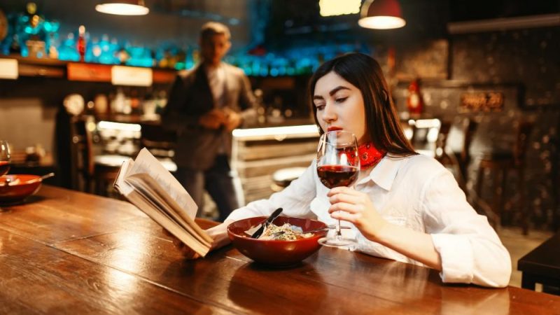 young-woman-drinks-red-wine-and-reading-book-at-wooden-bar-counter-female-customer-relaxing-in-pub